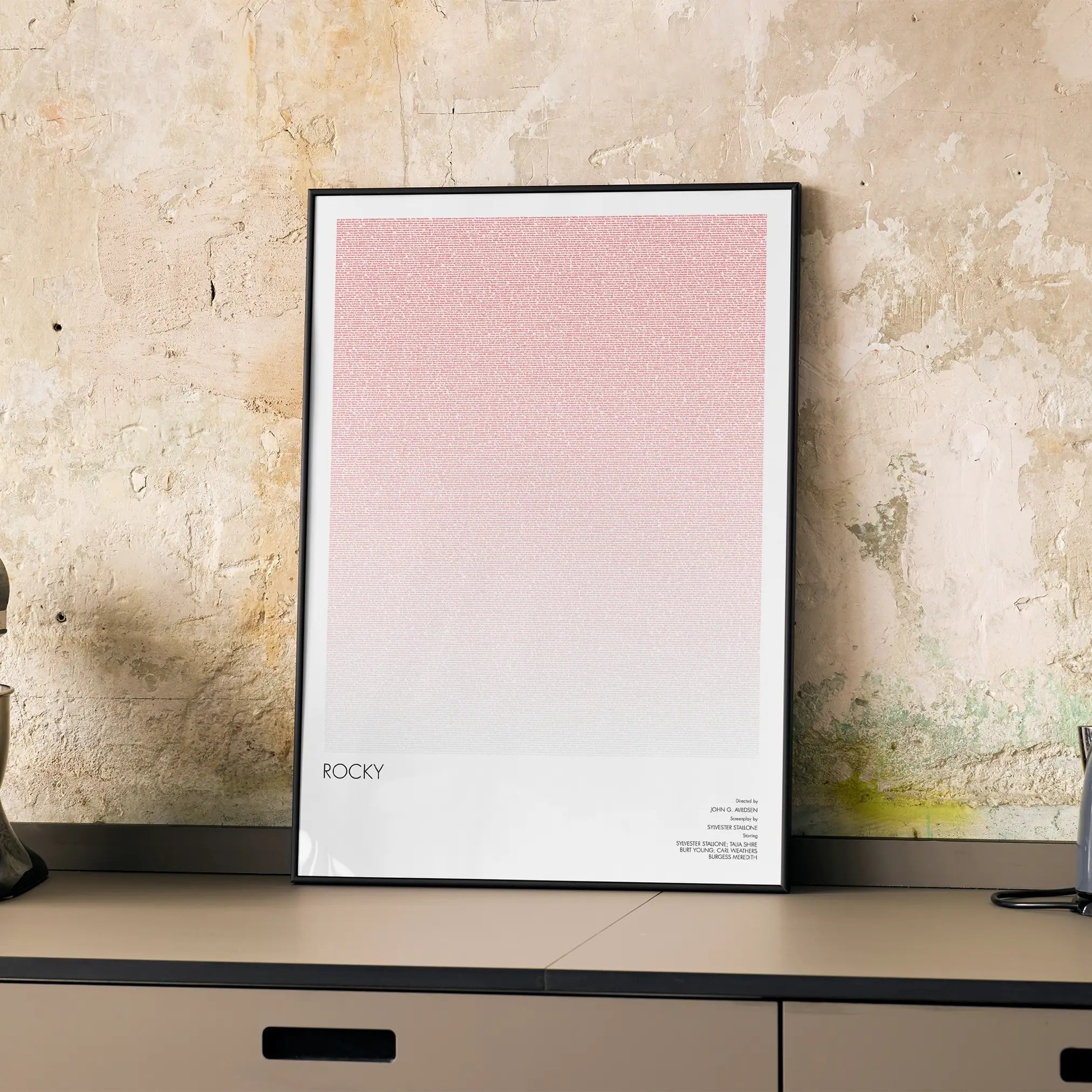 A framed Rocky movie script poster displayed on a cabinet in a minimalist interior.