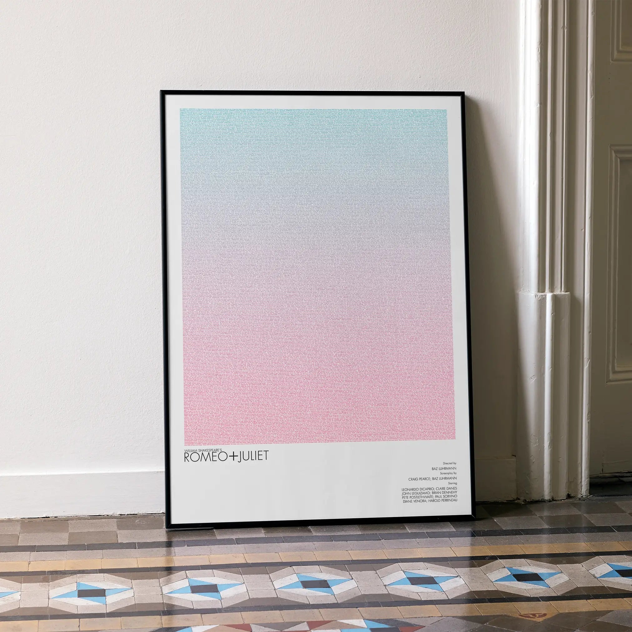 A framed Romeo + Juliet movie script poster leaning against a wall in a minimalist interior.
