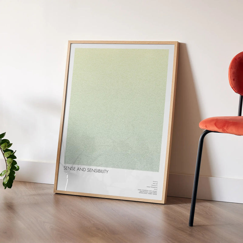 Framed Sense and Sensibility poster leaning against a wall with a chair and plant in the background