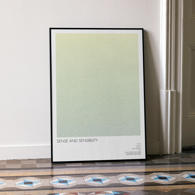Framed poster with 'Sense and Sensibility' text on a light green background, leaning against a wall.