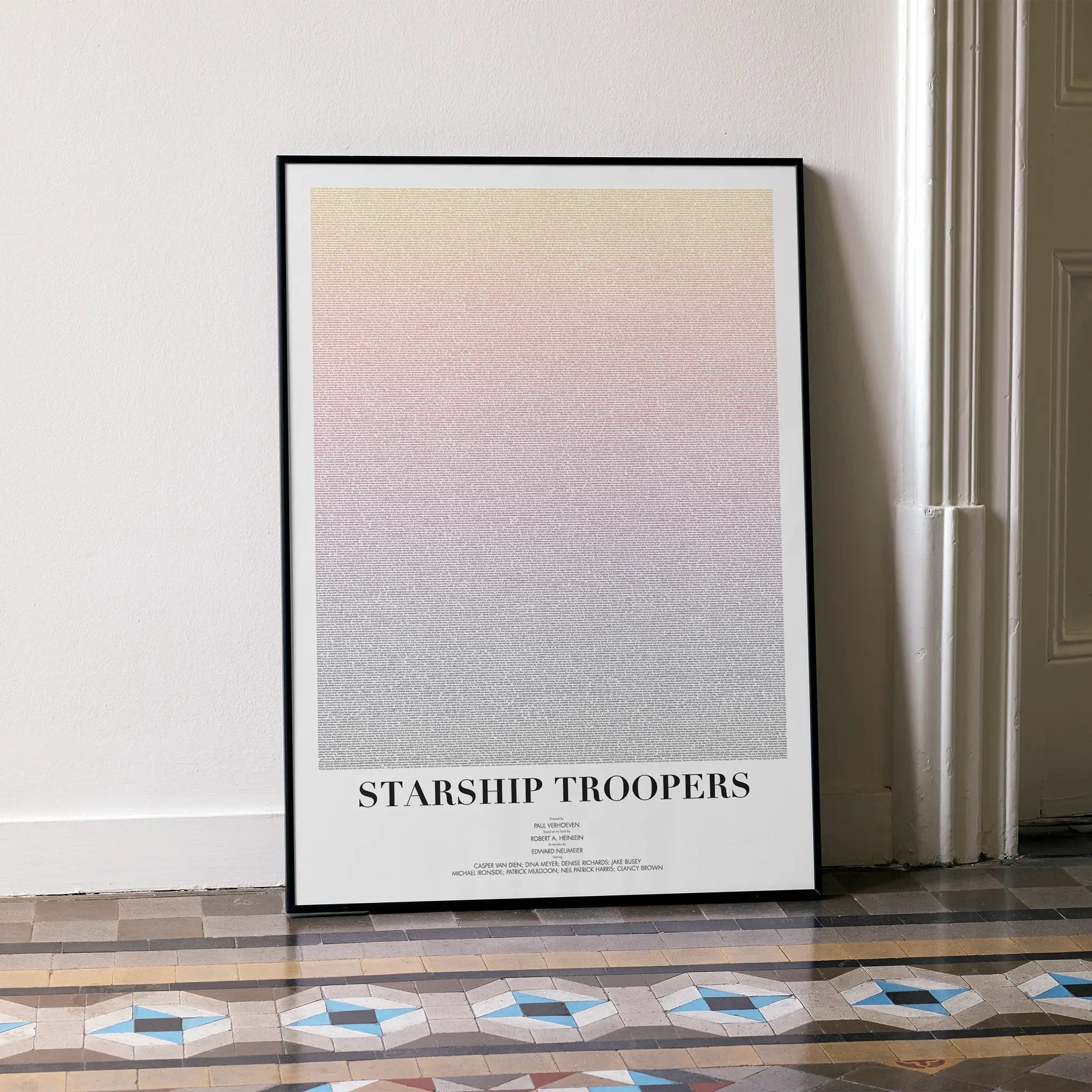 A framed Starship Troopers movie script poster leaning against a wall in a minimalist interior.