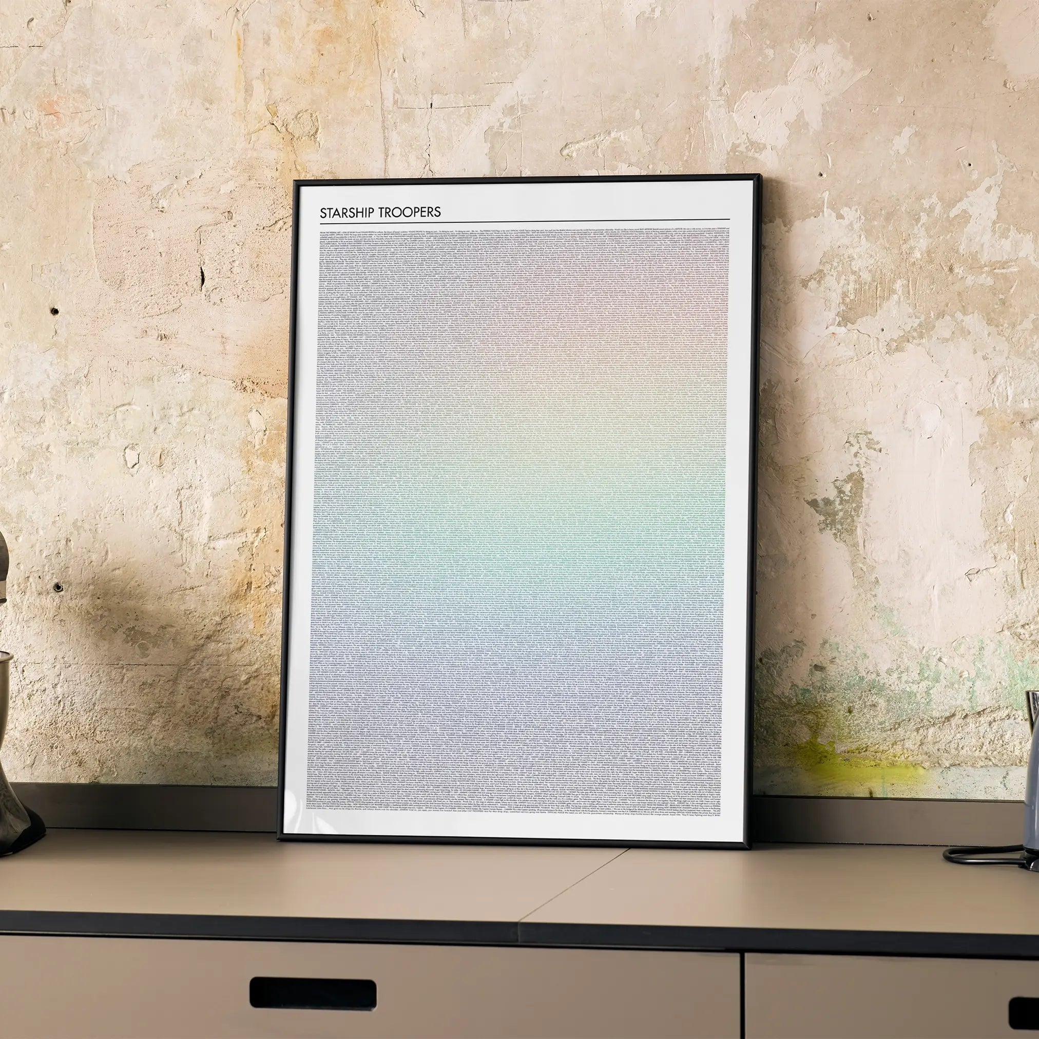 A framed Starship Troopers movie script poster displayed on a cabinet in a minimalist interior.