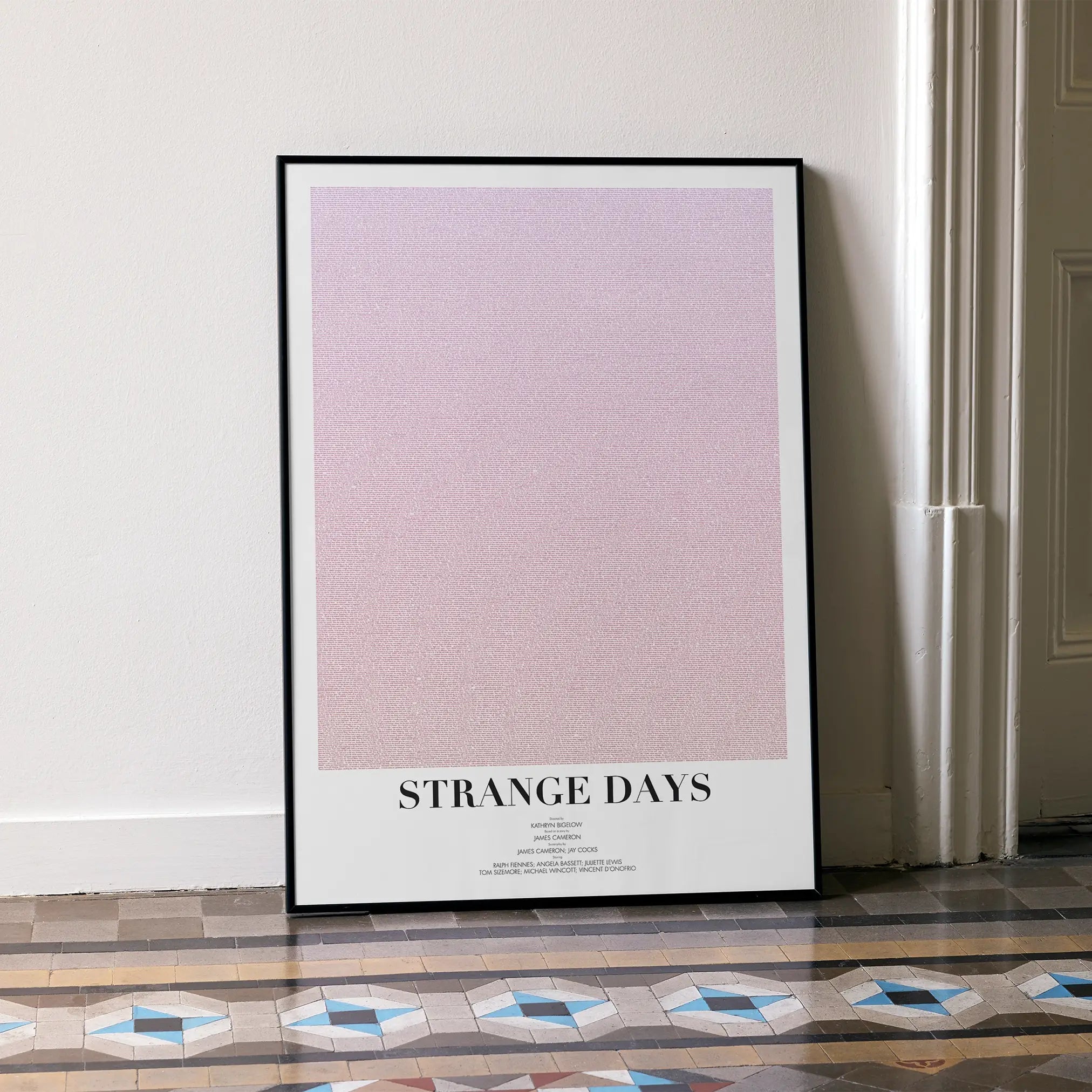 A framed Strange Days movie script poster leaning against a wall in a minimalist interior.
