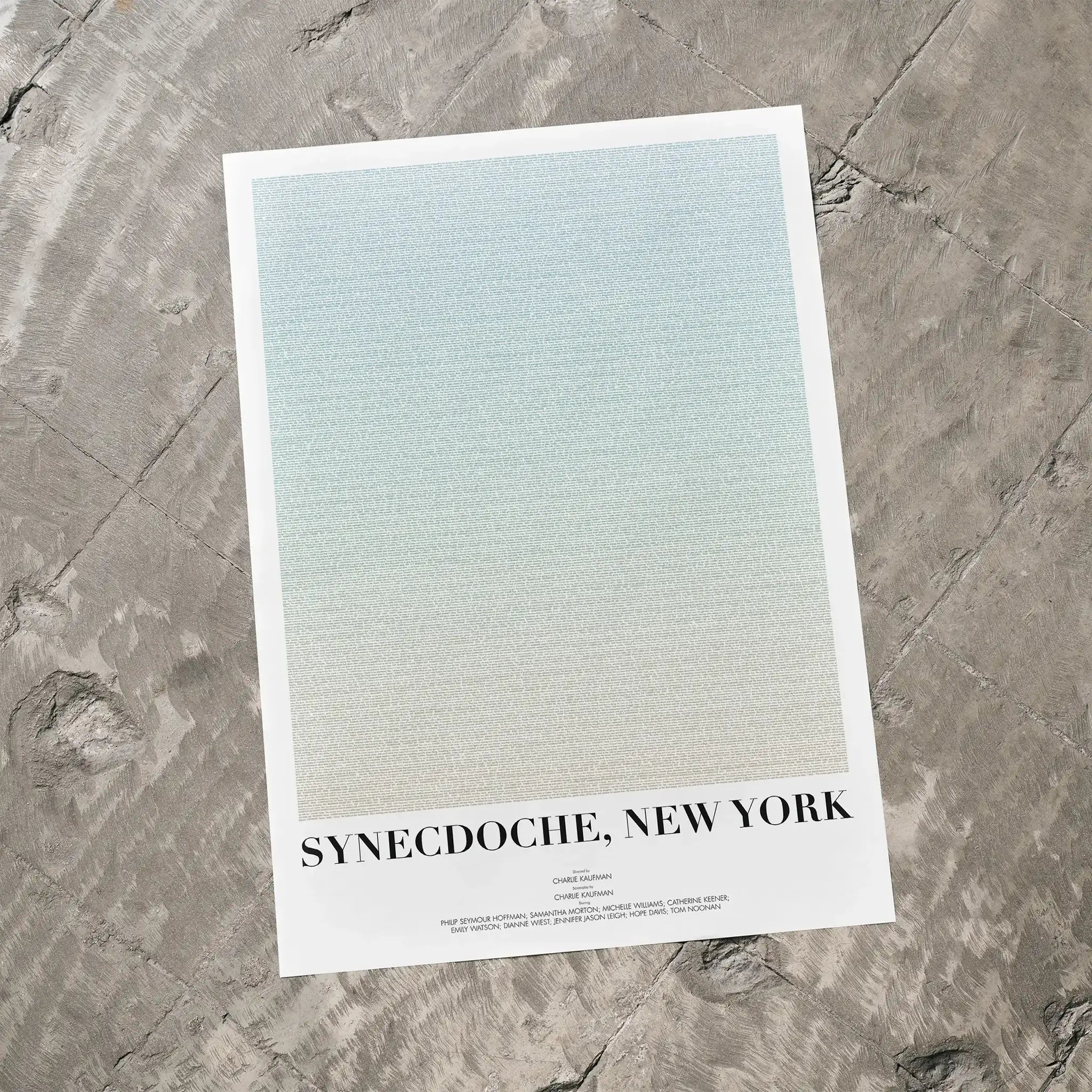 A Synecdoche, New York movie script poster laid flat on a textured floor surface.