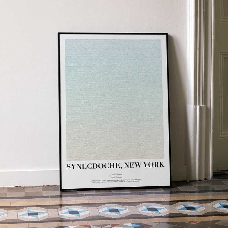 A framed Synecdoche, New York movie script poster leaning against a wall in a minimalist interior.