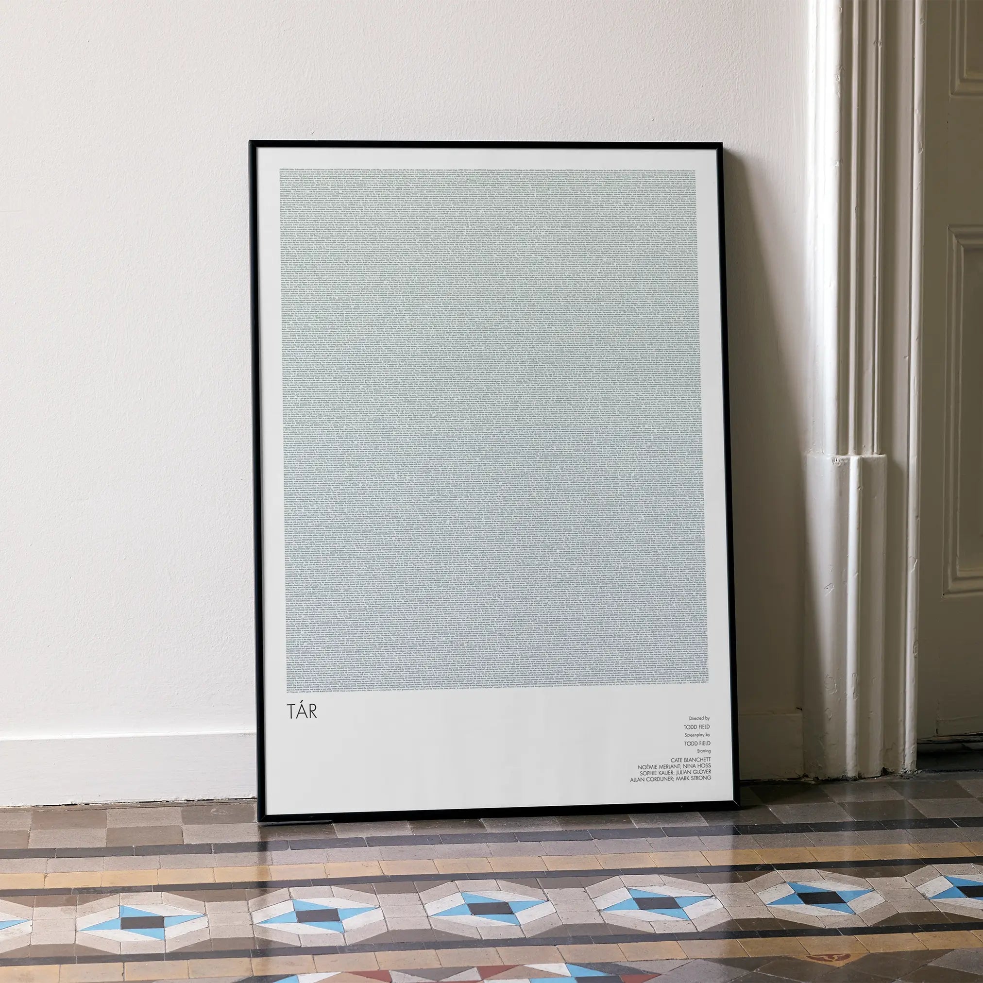 A framed Tár movie script poster leaning against a wall in a minimalist interior.
