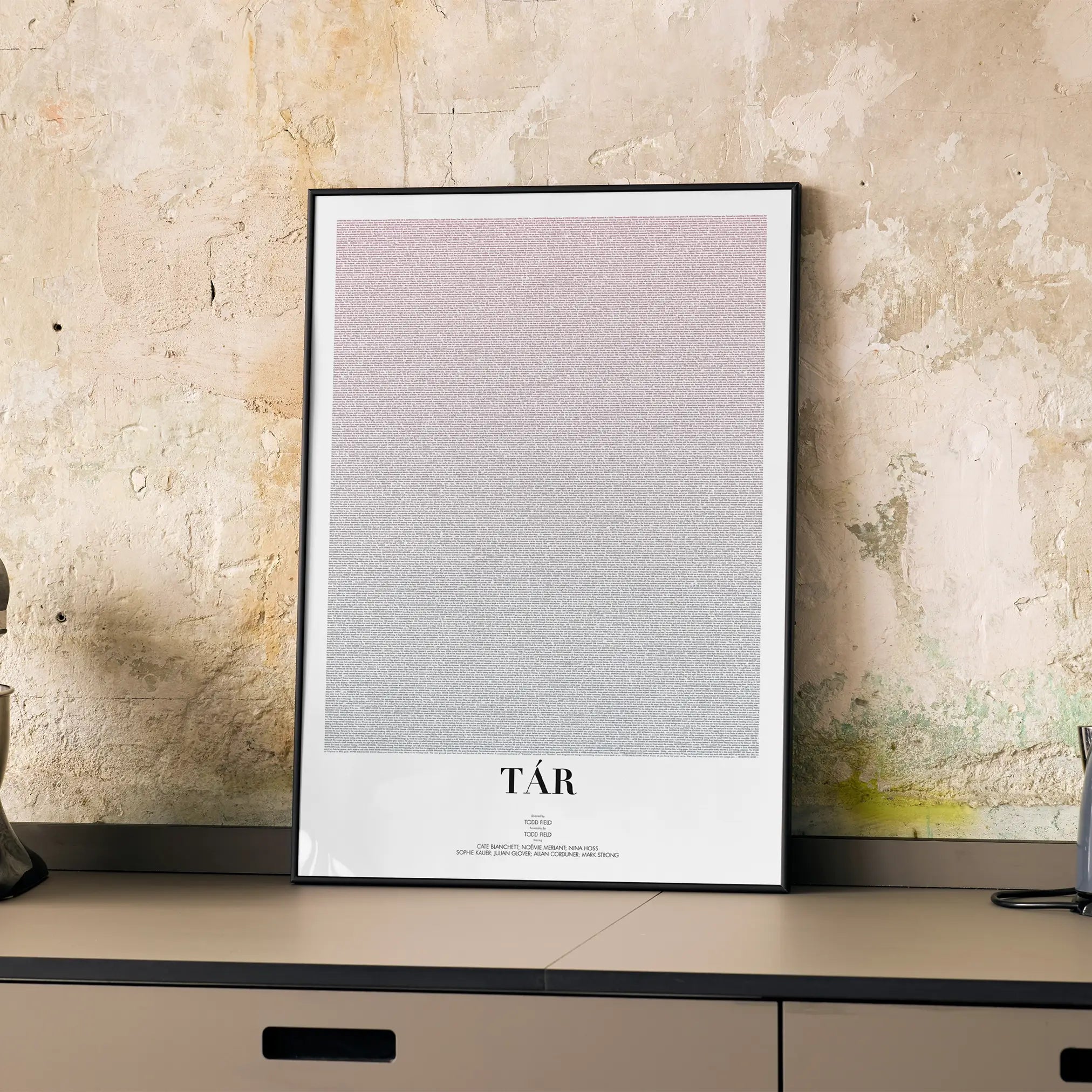 A framed Tár movie script poster displayed on a cabinet in a minimalist interior.