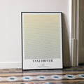 A framed Taxi Driver movie script poster leaning against a wall in a minimalist interior.