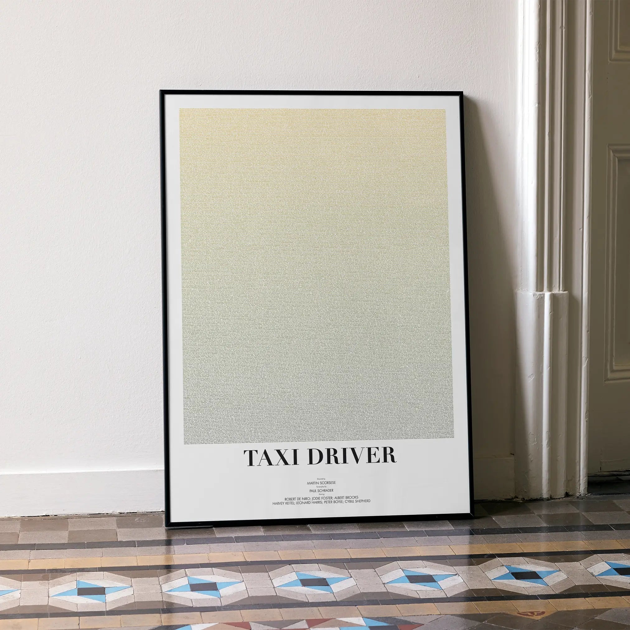 A framed Taxi Driver movie script poster leaning against a wall in a minimalist interior.