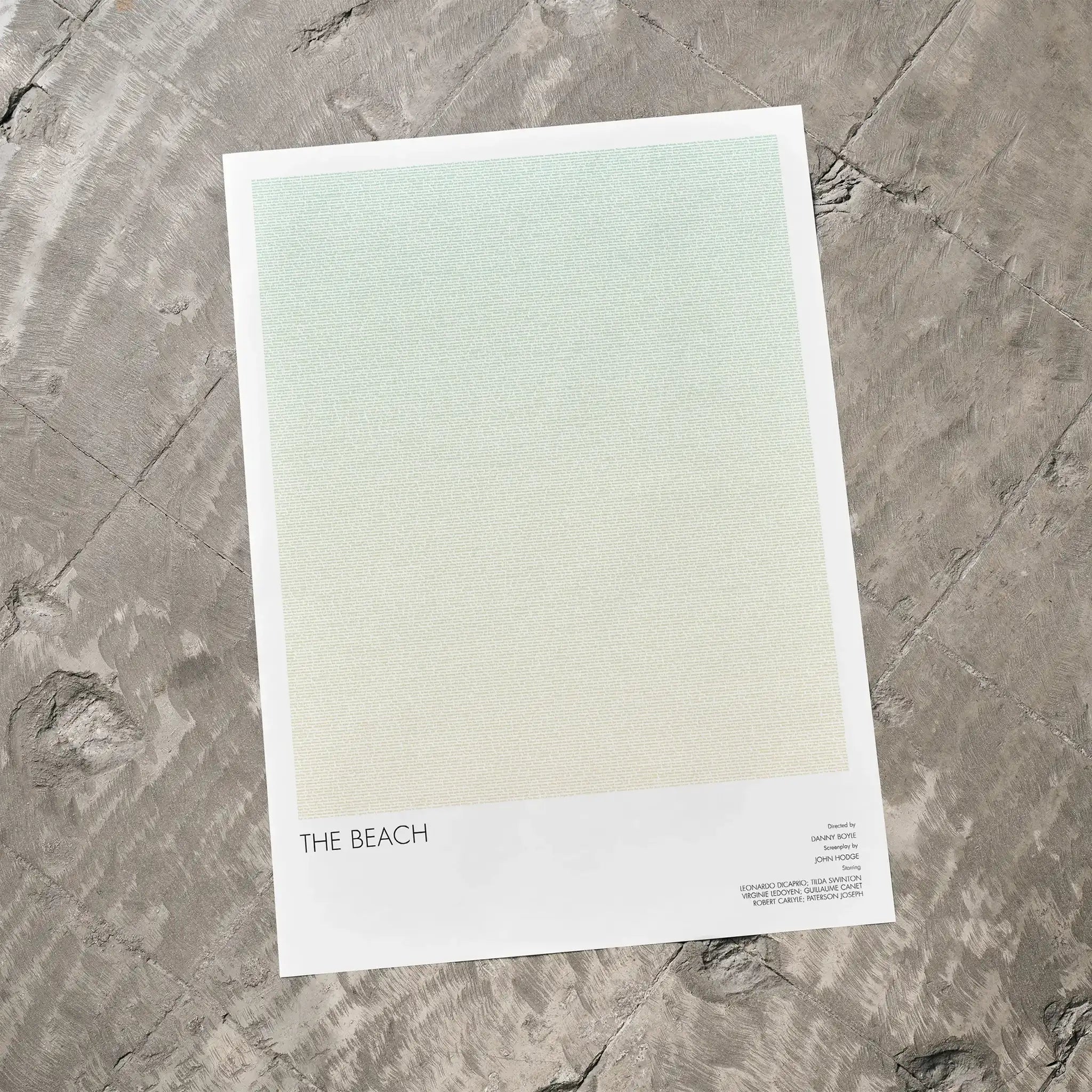 A The Beach movie script poster laid flat on a textured floor surface.