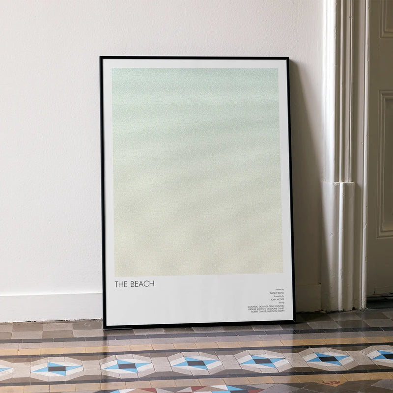 A framed The Beach movie script poster leaning against a wall in a minimalist interior.