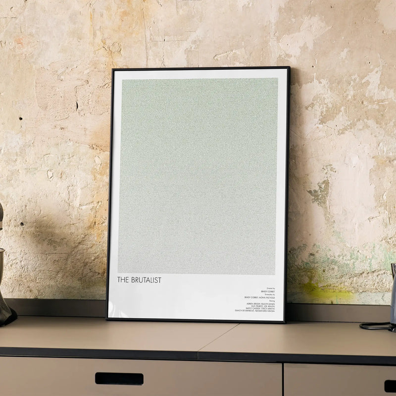 A framed The Brutalist movie script poster displayed on a cabinet in a minimalist interior.
