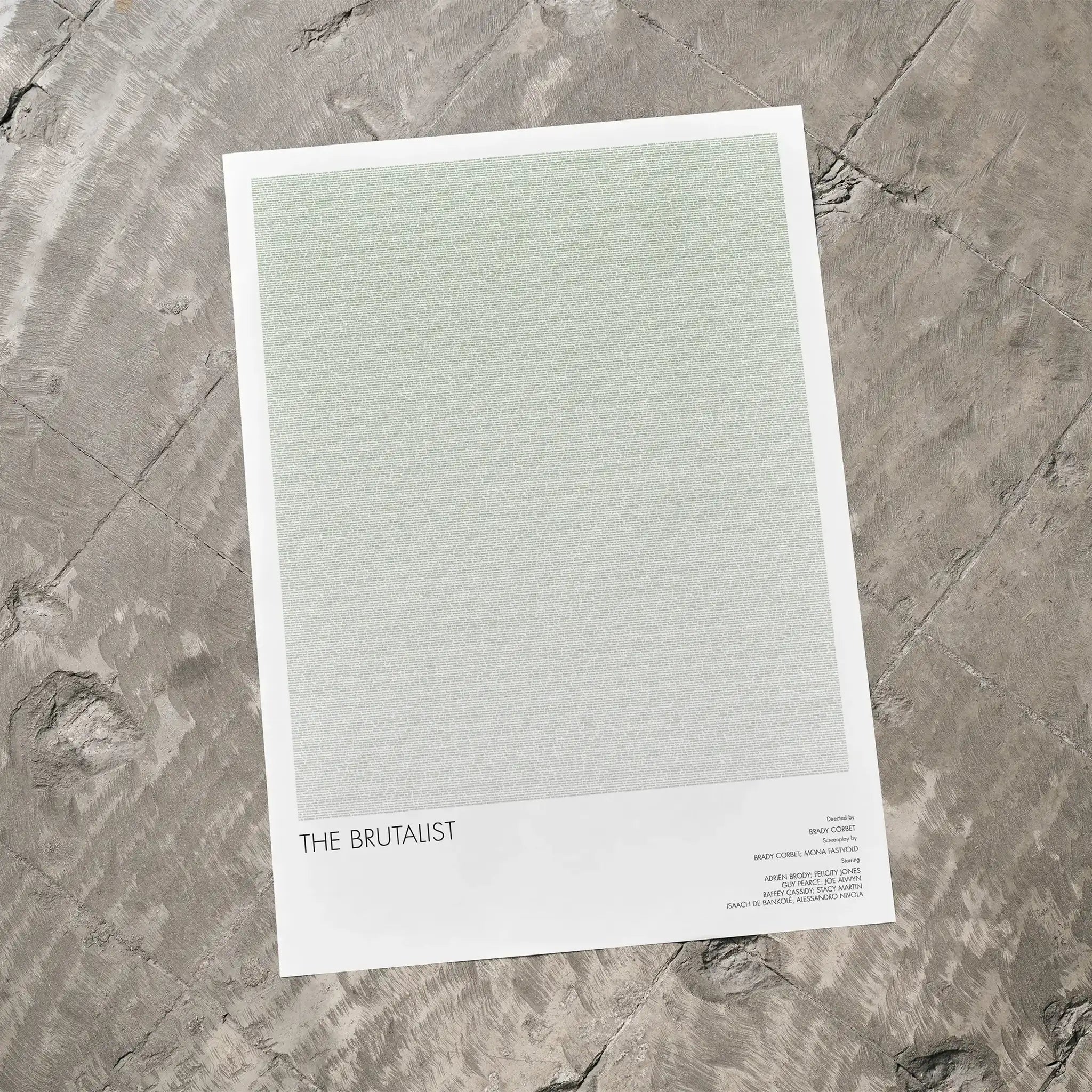 A The Brutalist movie script poster laid flat on a textured floor surface.