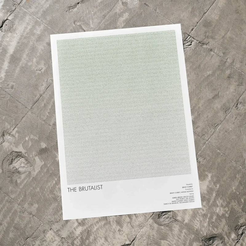 A The Brutalist movie script poster laid flat on a textured floor surface.