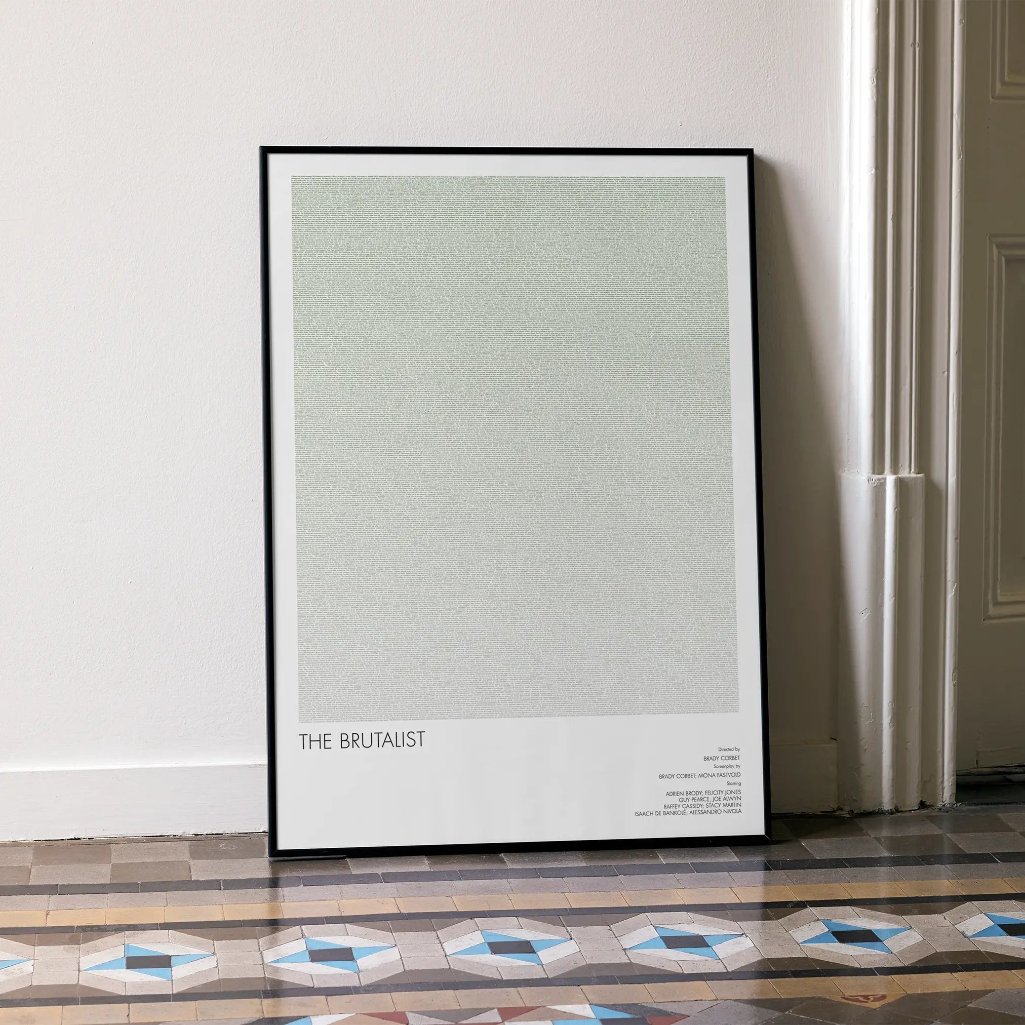 A framed The Brutalist movie script poster leaning against a wall in a minimalist interior.