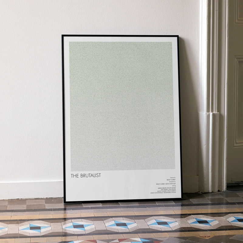 A framed The Brutalist movie script poster leaning against a wall in a minimalist interior.