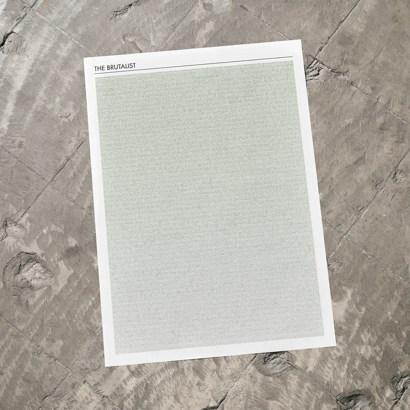 A The Brutalist movie script poster laid flat on a textured floor surface.