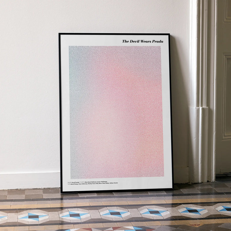A framed The Devil Wears Prada movie script poster leaning against a wall in a minimalist interior.