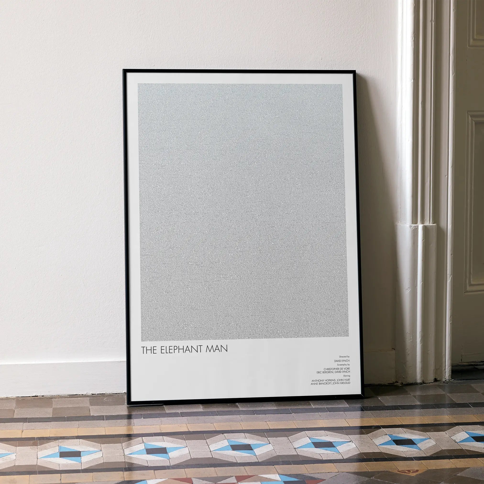 A framed The Elephant Man movie script poster leaning against a wall in a minimalist interior.