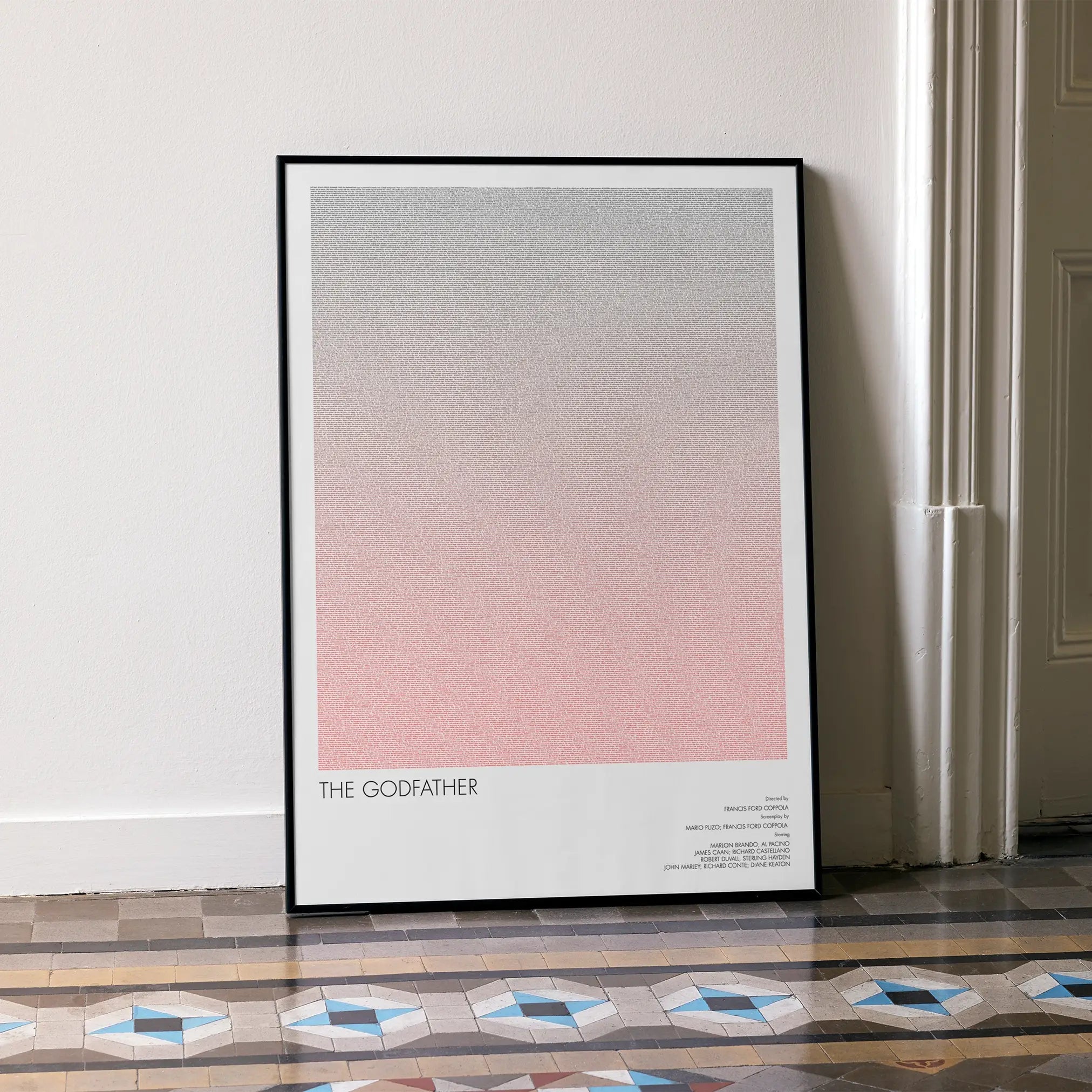 A framed The Godfather movie script poster leaning against a wall in a minimalist interior.