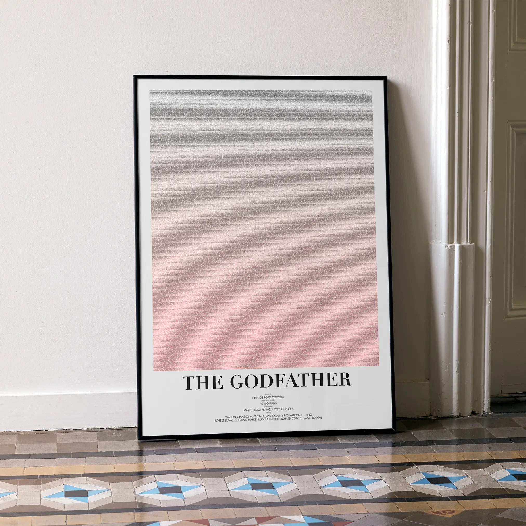A framed The Godfather movie script poster leaning against a wall in a minimalist interior.