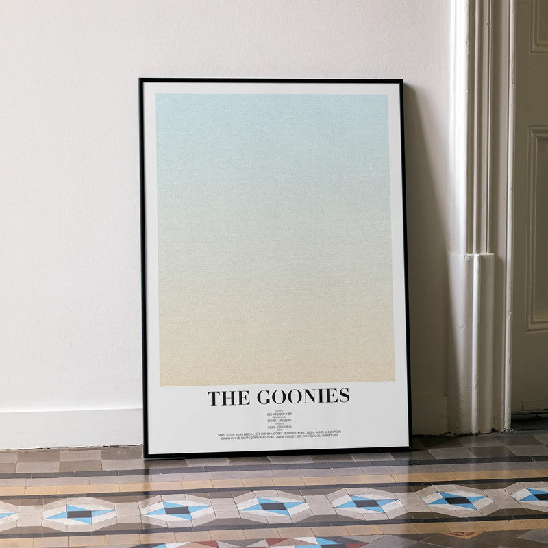 A large framed The Goonies movie script poster leaning against a white wall.