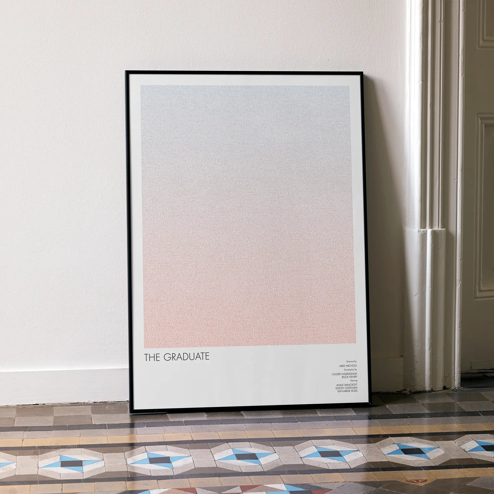 A framed The Graduate movie script poster leaning against a wall in a minimalist interior.