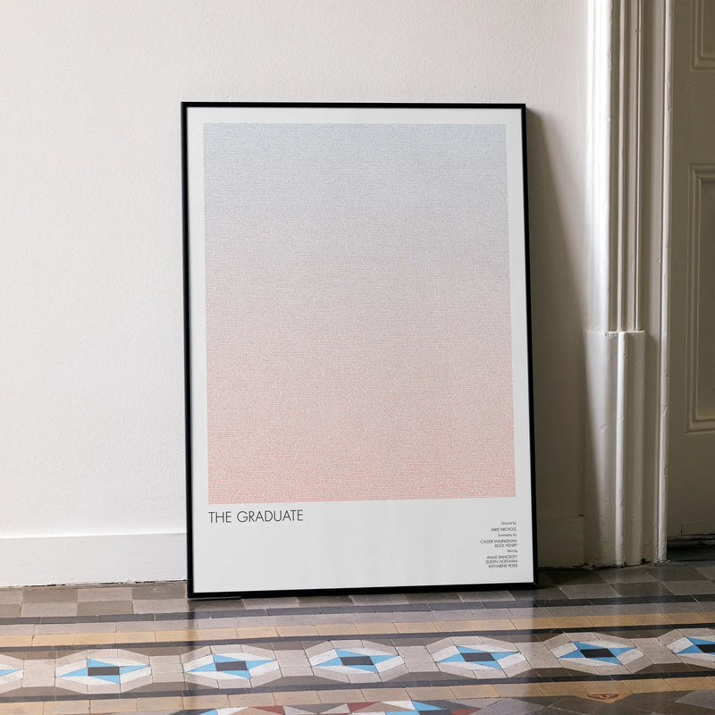 A framed The Graduate movie script poster leaning against a wall in a minimalist interior.