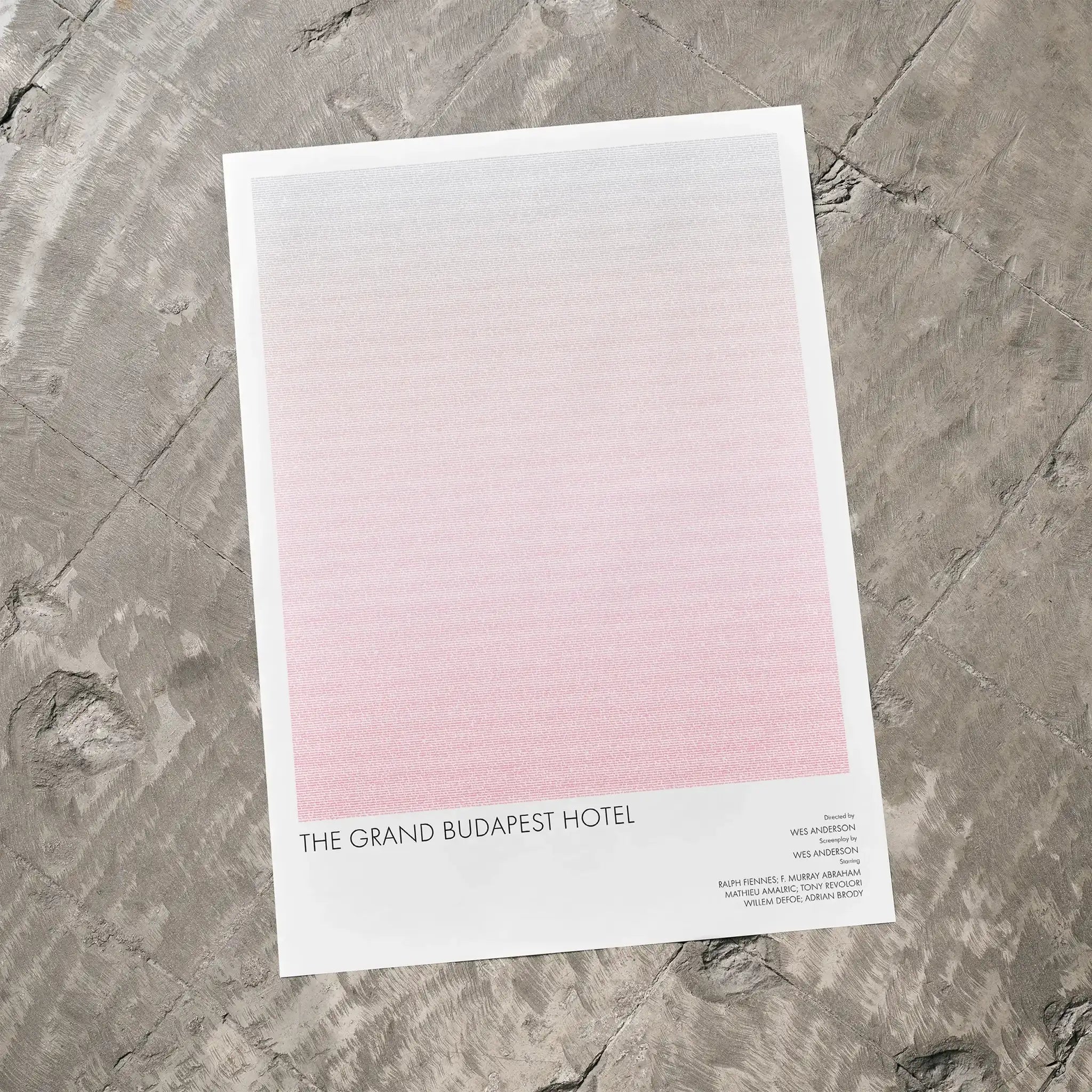 A The Grand Budapest Hotel movie script poster laid flat on a textured floor surface.