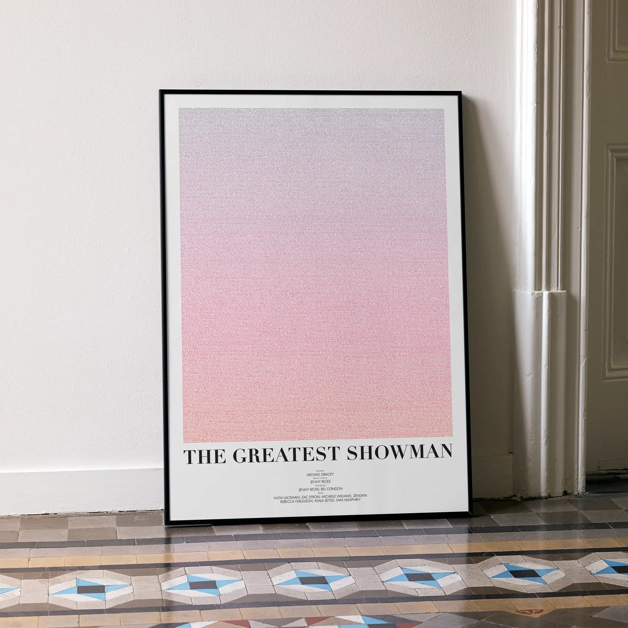 A framed The Greatest Showman movie script poster leaning against a wall in a minimalist interior.