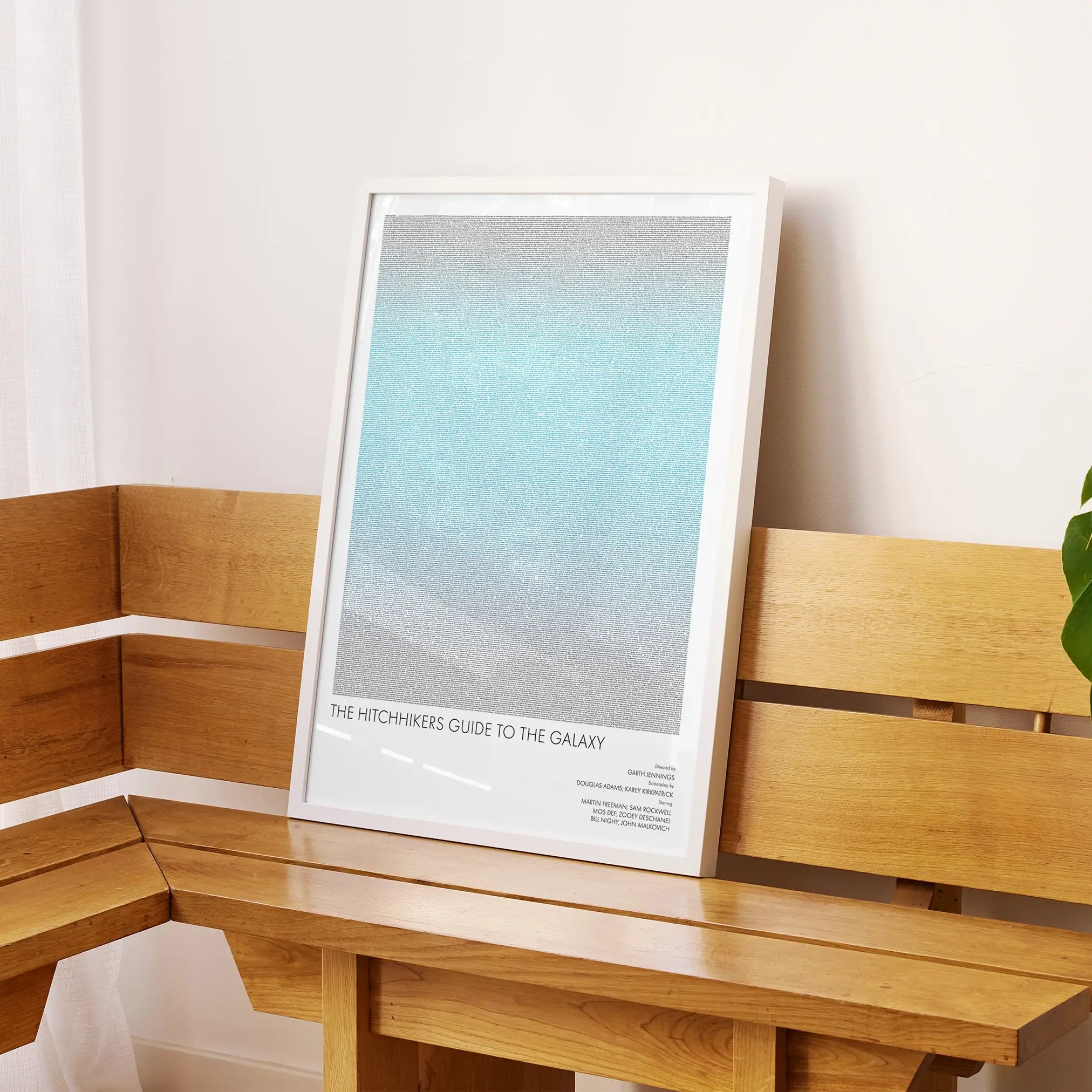 A framed The Hitchhiker's Guide to the Galaxy movie script poster displayed on a sideboard in a contemporary space.