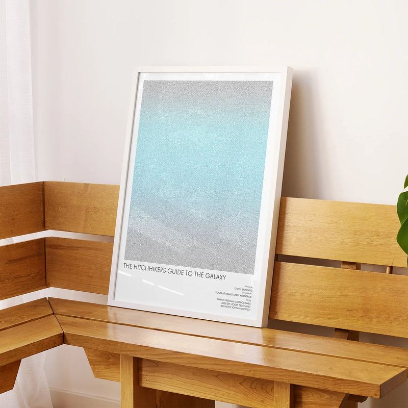A framed The Hitchhiker's Guide to the Galaxy movie script poster displayed on a sideboard in a contemporary space.