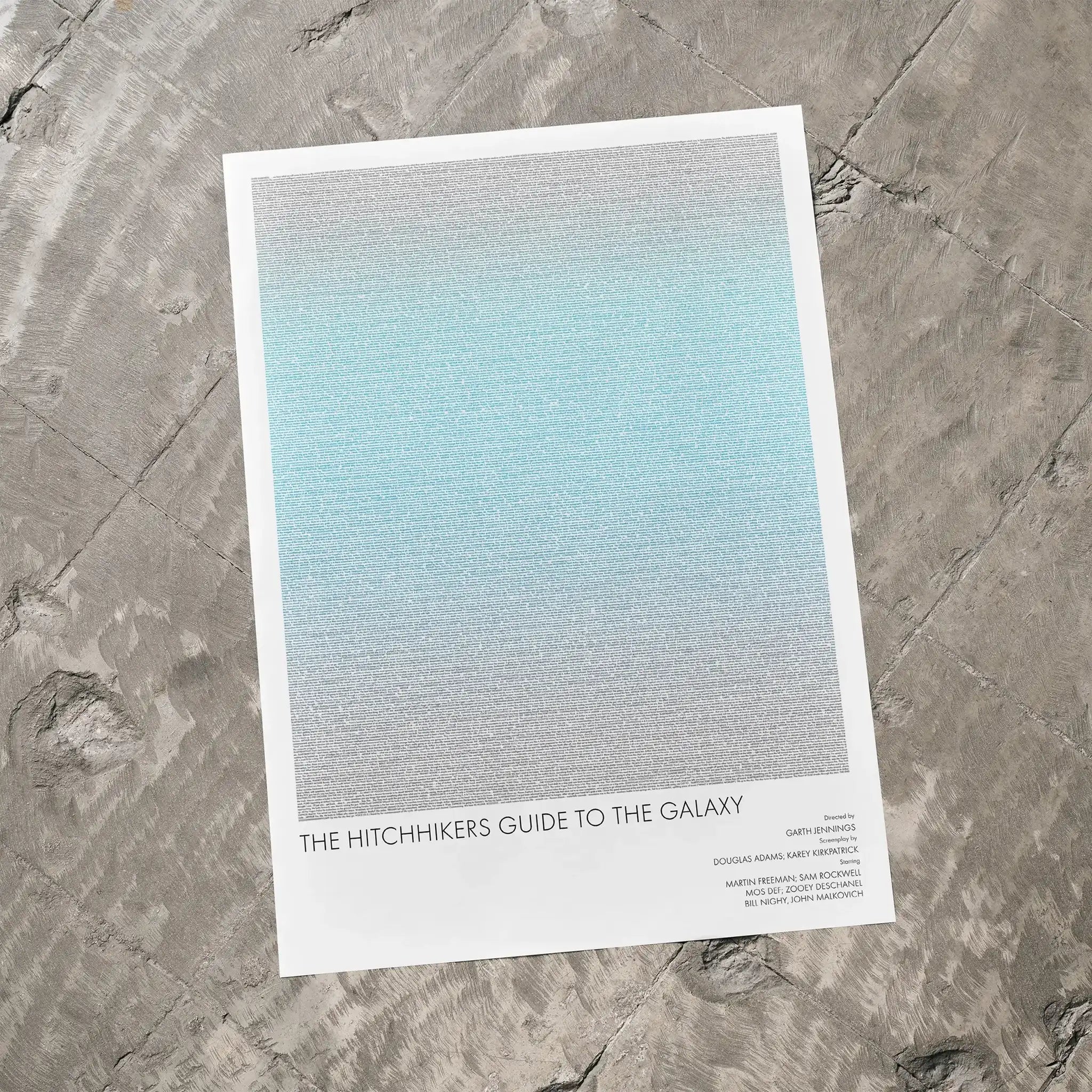 A The Hitchhiker's Guide to the Galaxy movie script poster laid flat on a textured floor surface.
