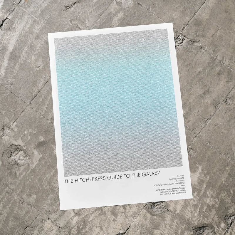 A The Hitchhiker's Guide to the Galaxy movie script poster laid flat on a textured floor surface.