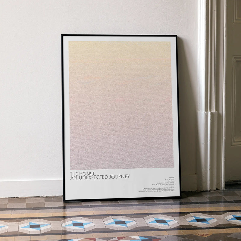 A framed The Hobbit: An Unexpected Journey movie script poster leaning against a wall in a minimalist interior.