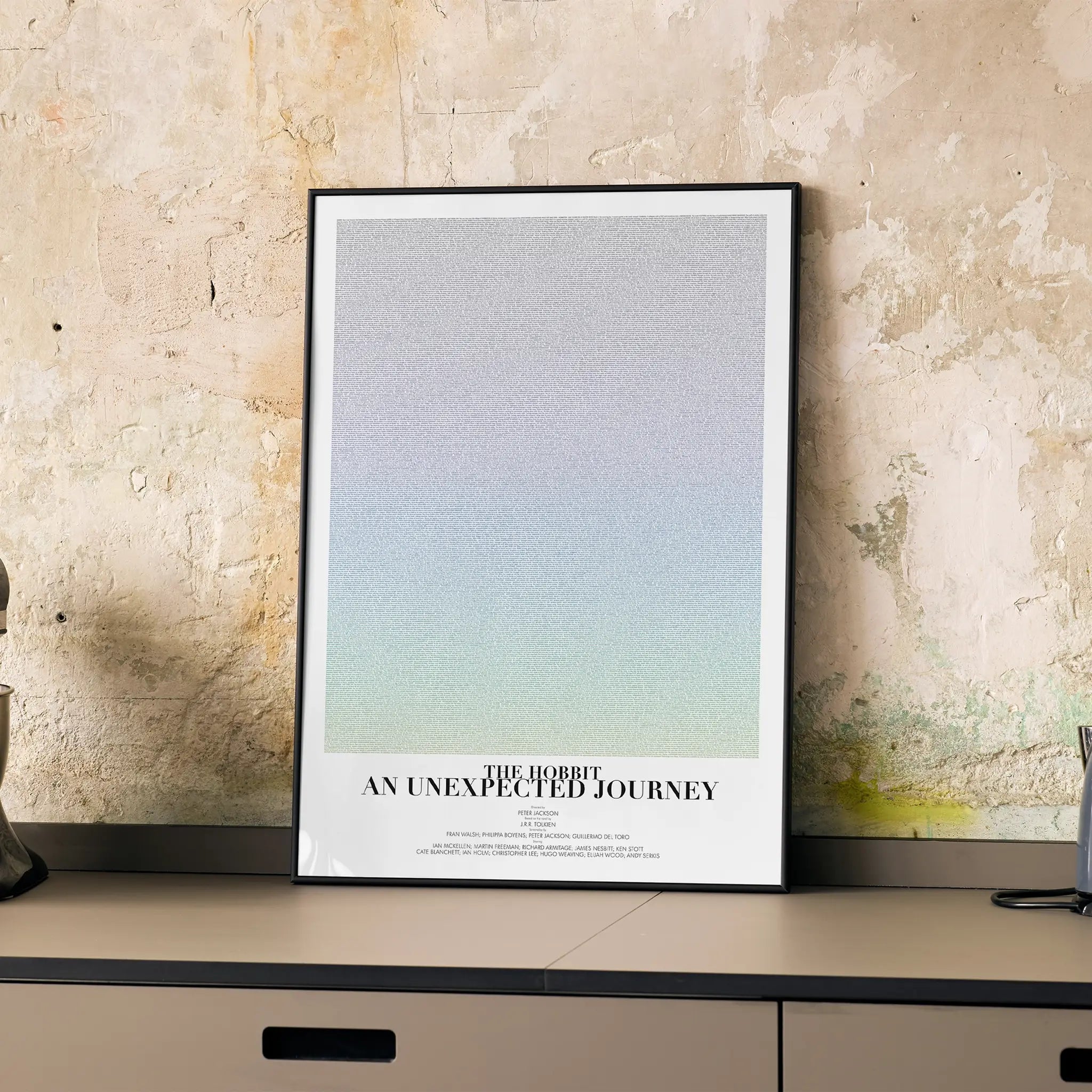 A framed The Hobbit: An Unexpected Journey movie script poster displayed on a cabinet in a minimalist interior.