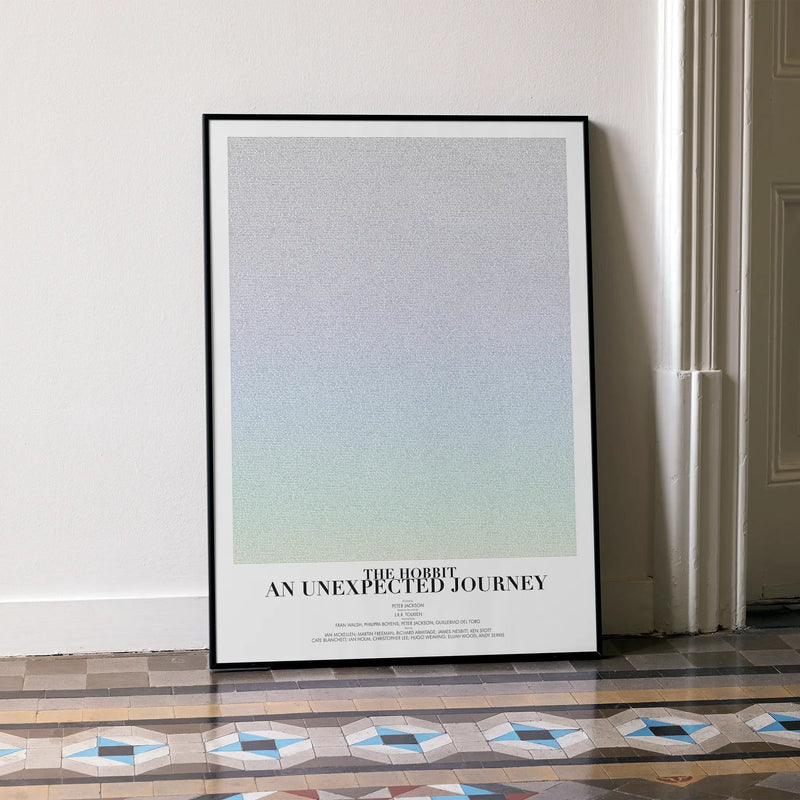A framed The Hobbit: An Unexpected Journey movie script poster leaning against a wall in a minimalist interior.