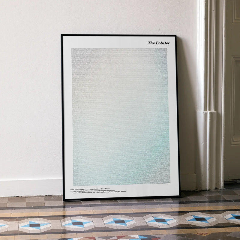 A framed The Lobster movie script poster leaning against a wall in a minimalist interior.
