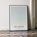 A framed The Lobster movie script poster leaning against a wall in a minimalist interior.