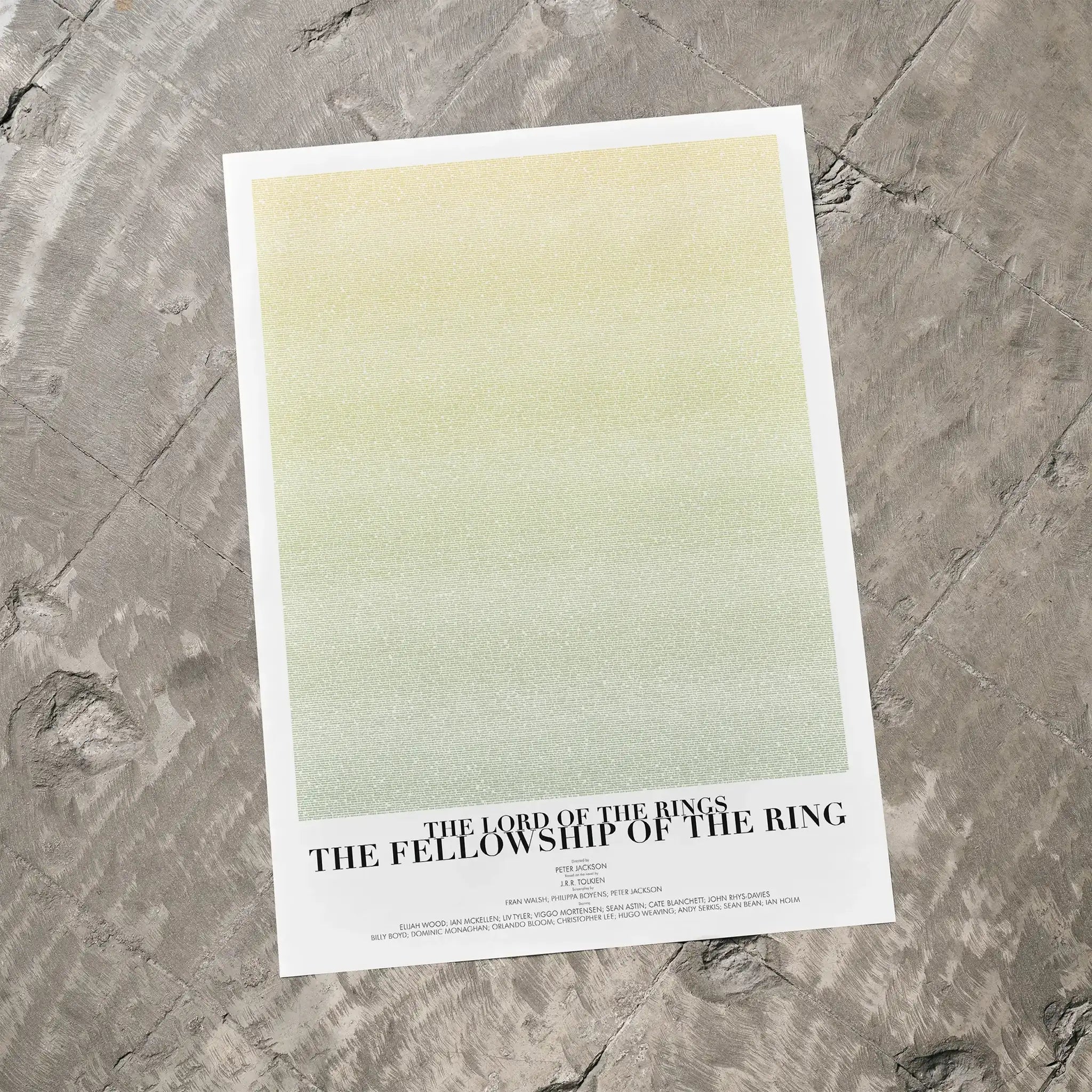 A The Lord of the Rings: The Fellowship of the Ring movie script poster laid flat on a textured floor surface.