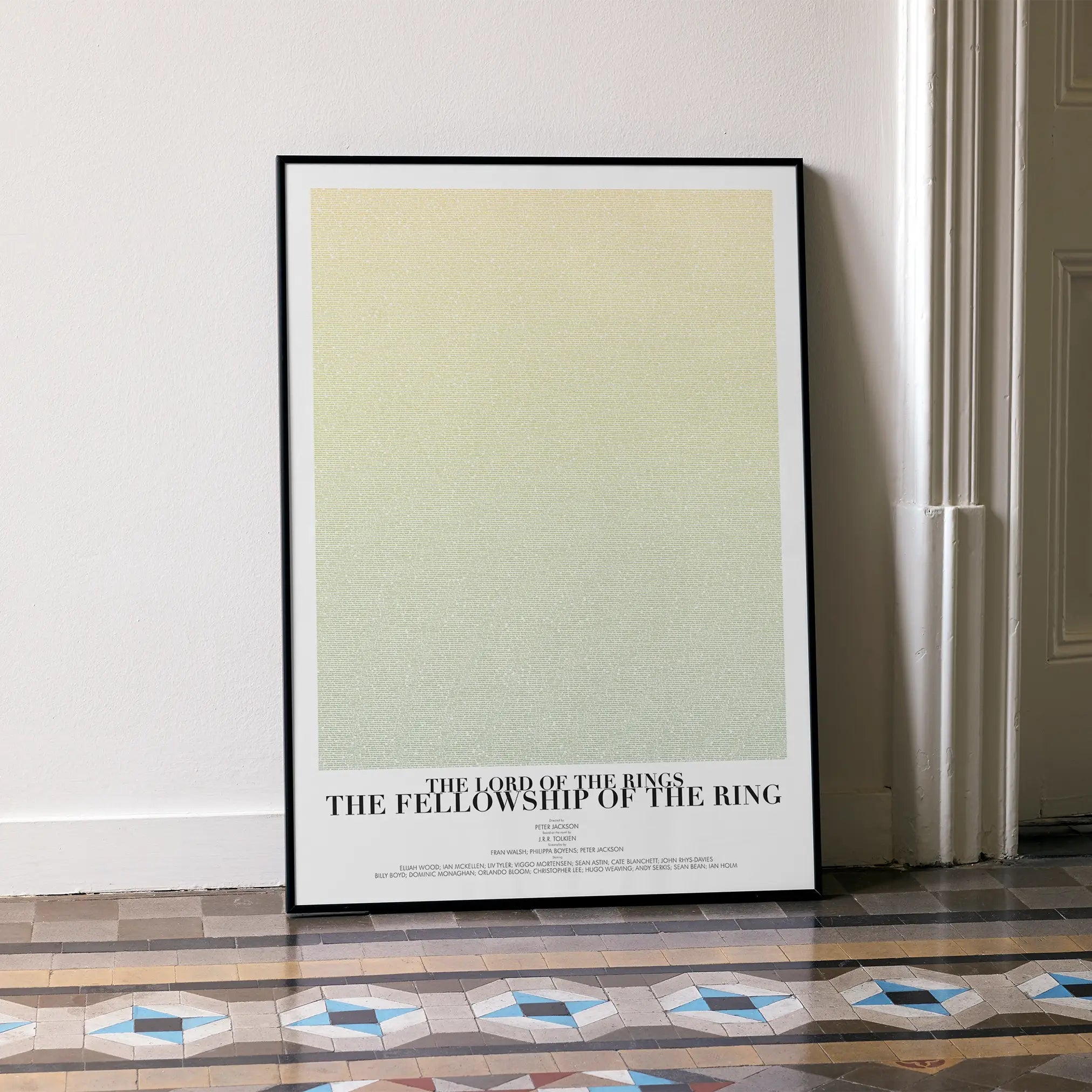 A framed The Lord of the Rings: The Fellowship of the Ring movie script poster leaning against a wall in a minimalist interior.