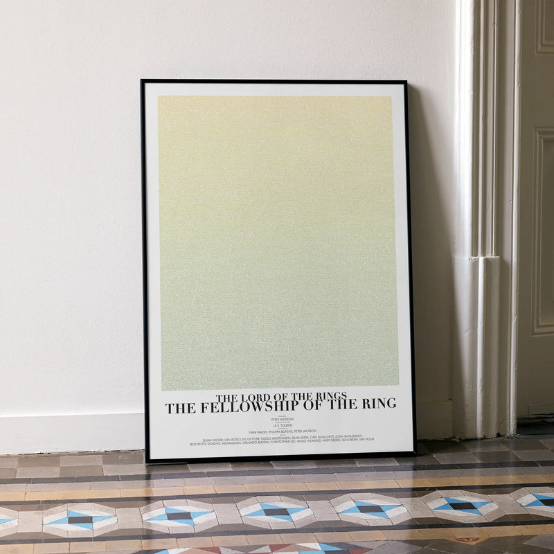 A framed The Lord of the Rings: The Fellowship of the Ring movie script poster leaning against a wall in a minimalist interior.