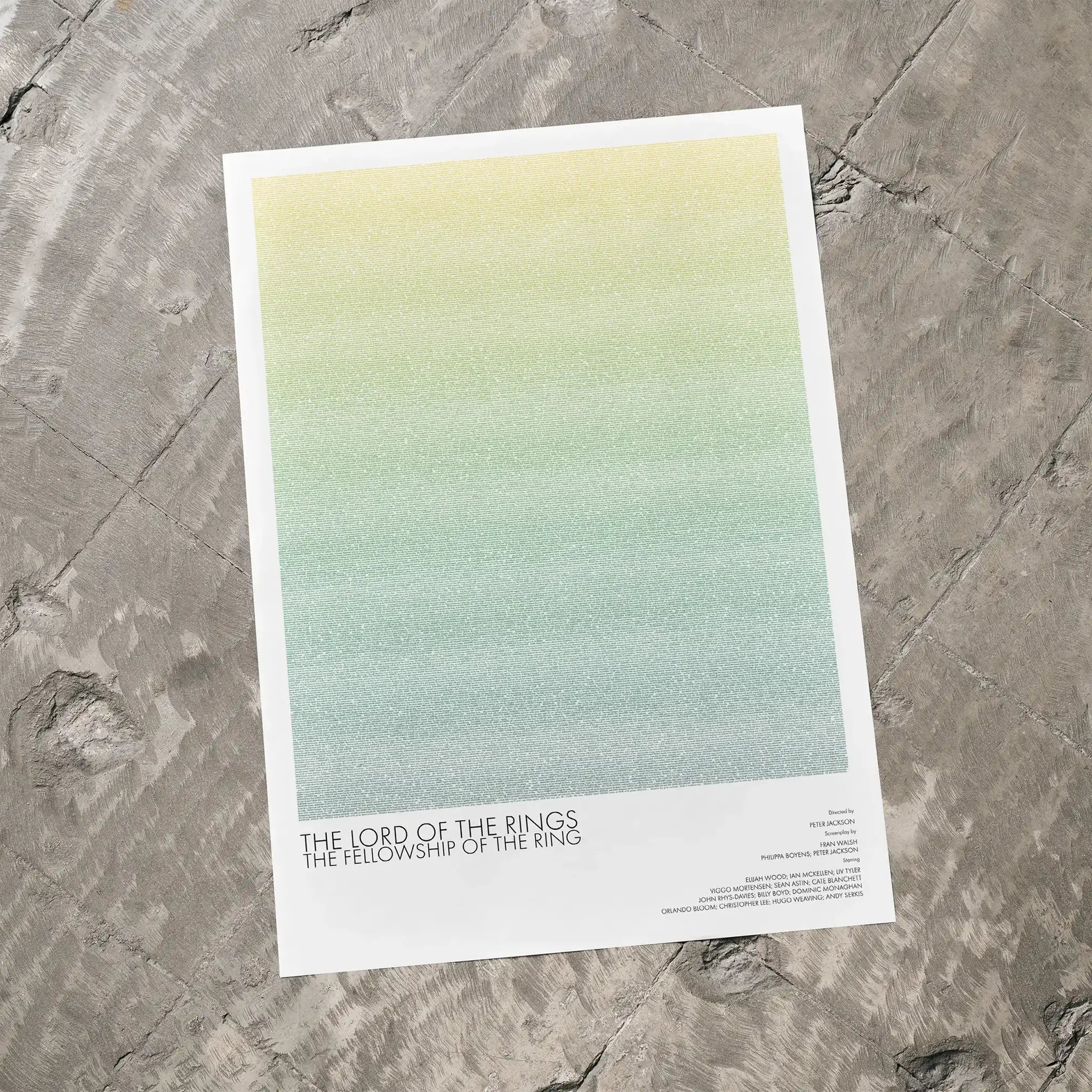 A The Lord of the Rings: The Fellowship of the Ring movie script poster laid flat on a textured floor surface.