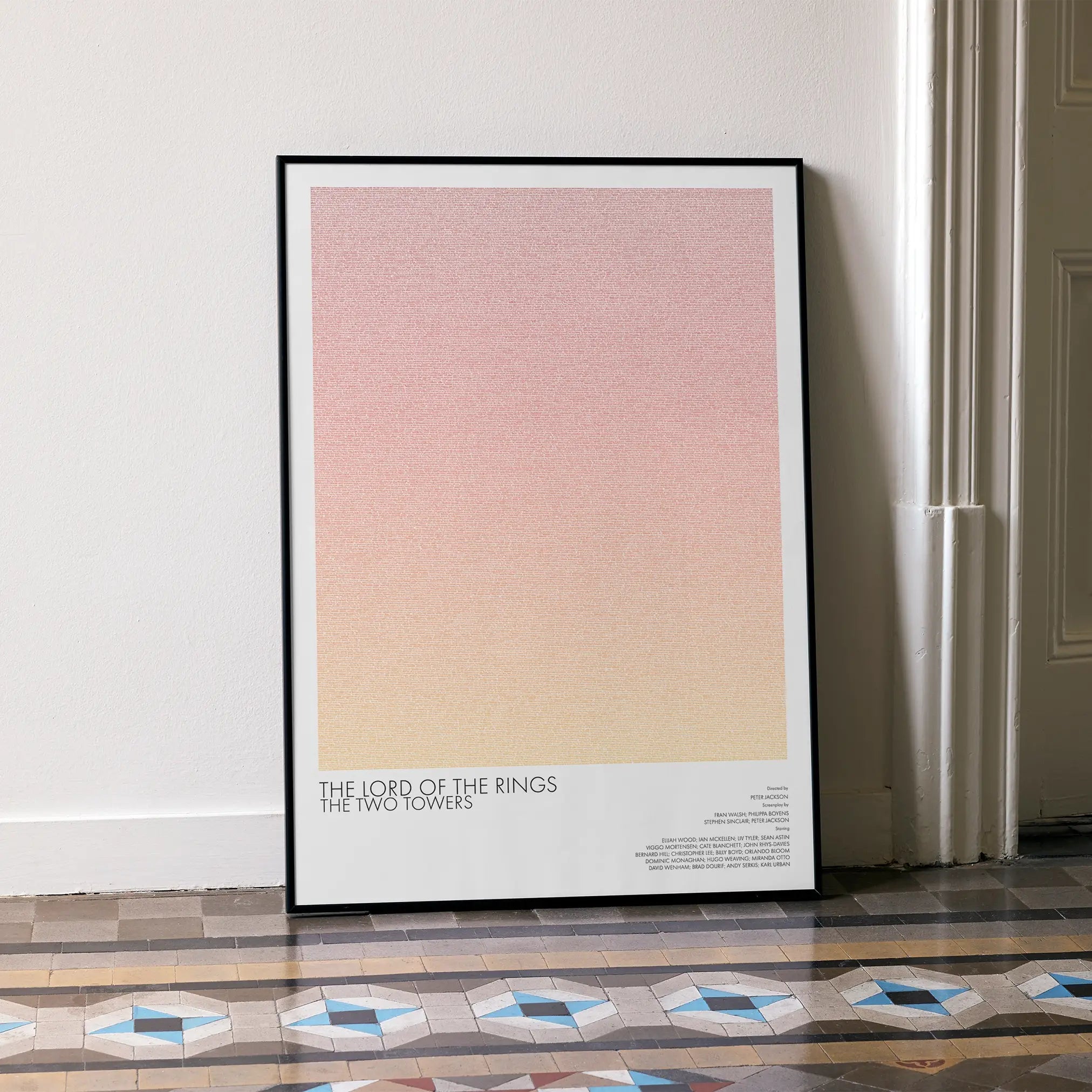 A framed The Lord of the Rings: The Two Towers movie script poster leaning against a wall in a minimalist interior.