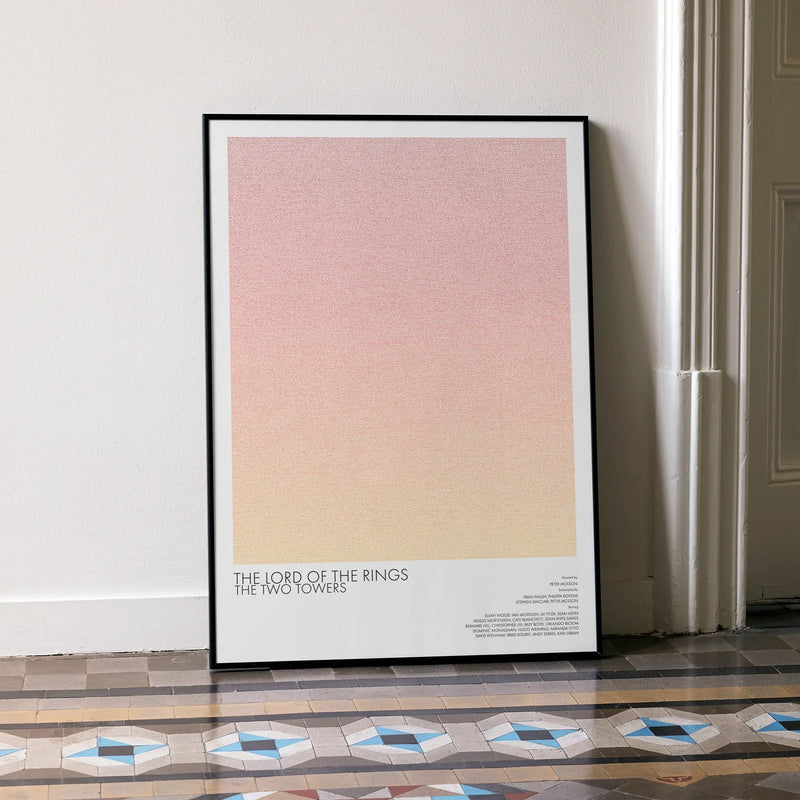 A framed The Lord of the Rings: The Two Towers movie script poster leaning against a wall in a minimalist interior.