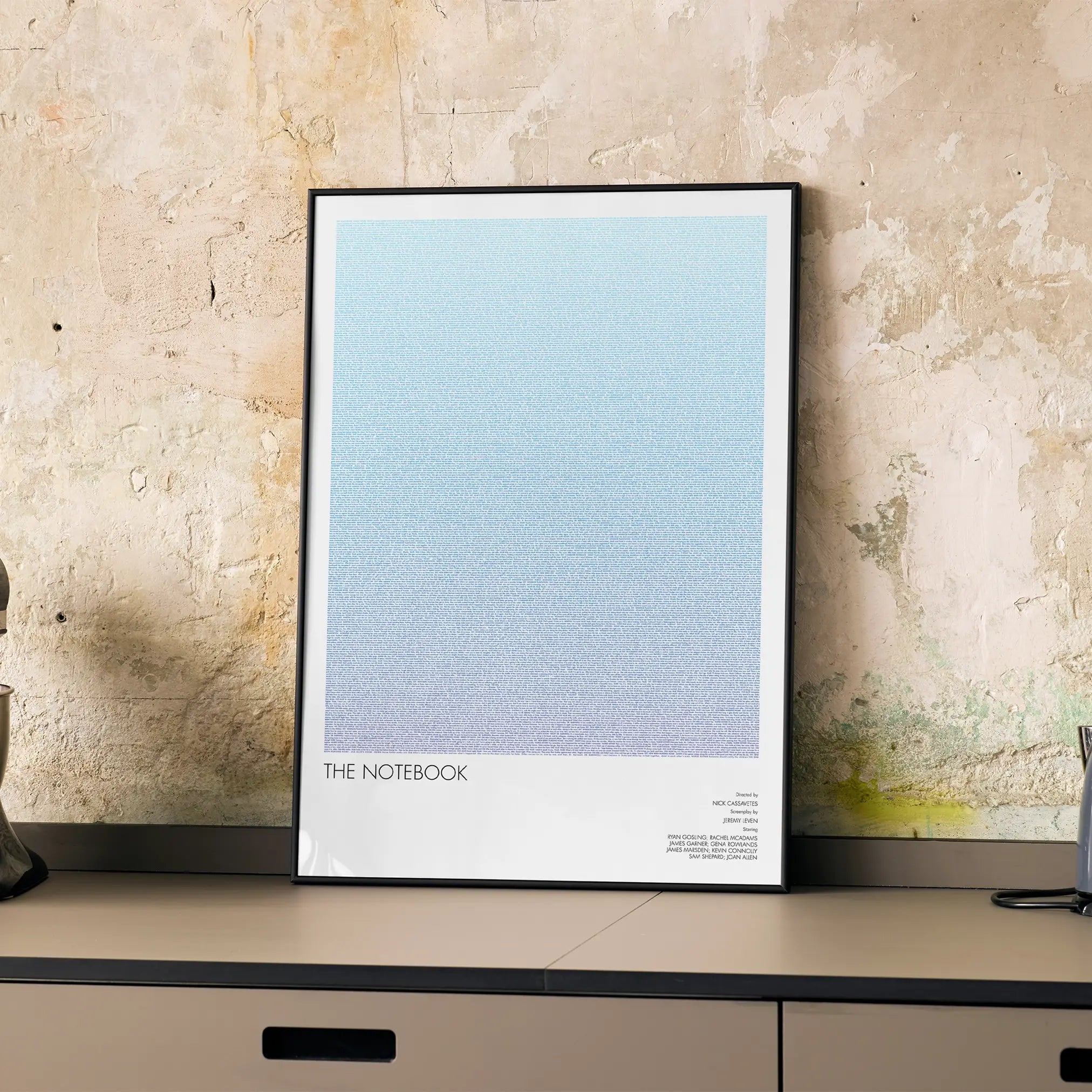 A framed The Notebook movie script poster displayed on a cabinet in a minimalist interior.