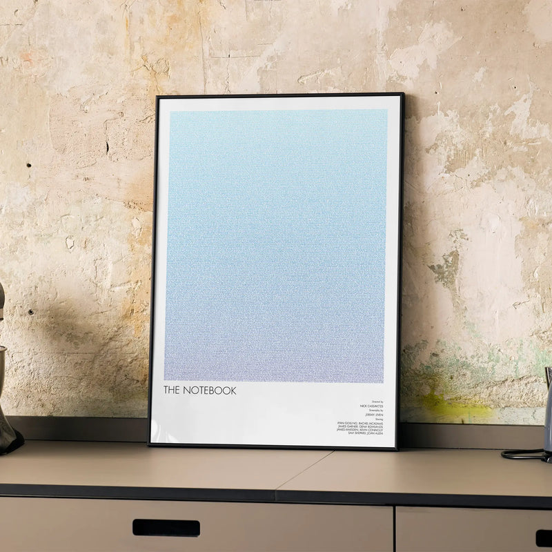 A framed The Notebook movie script poster displayed on a cabinet in a minimalist interior.
