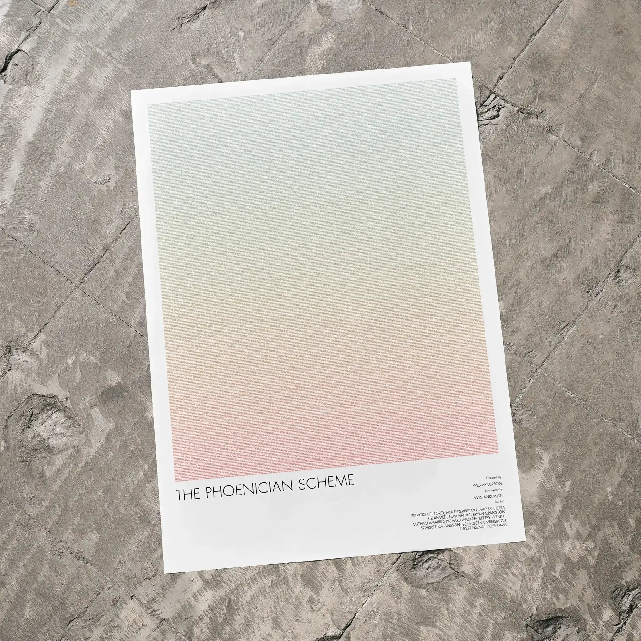 A The Phoenician Scheme movie script poster laid flat on a textured floor surface.