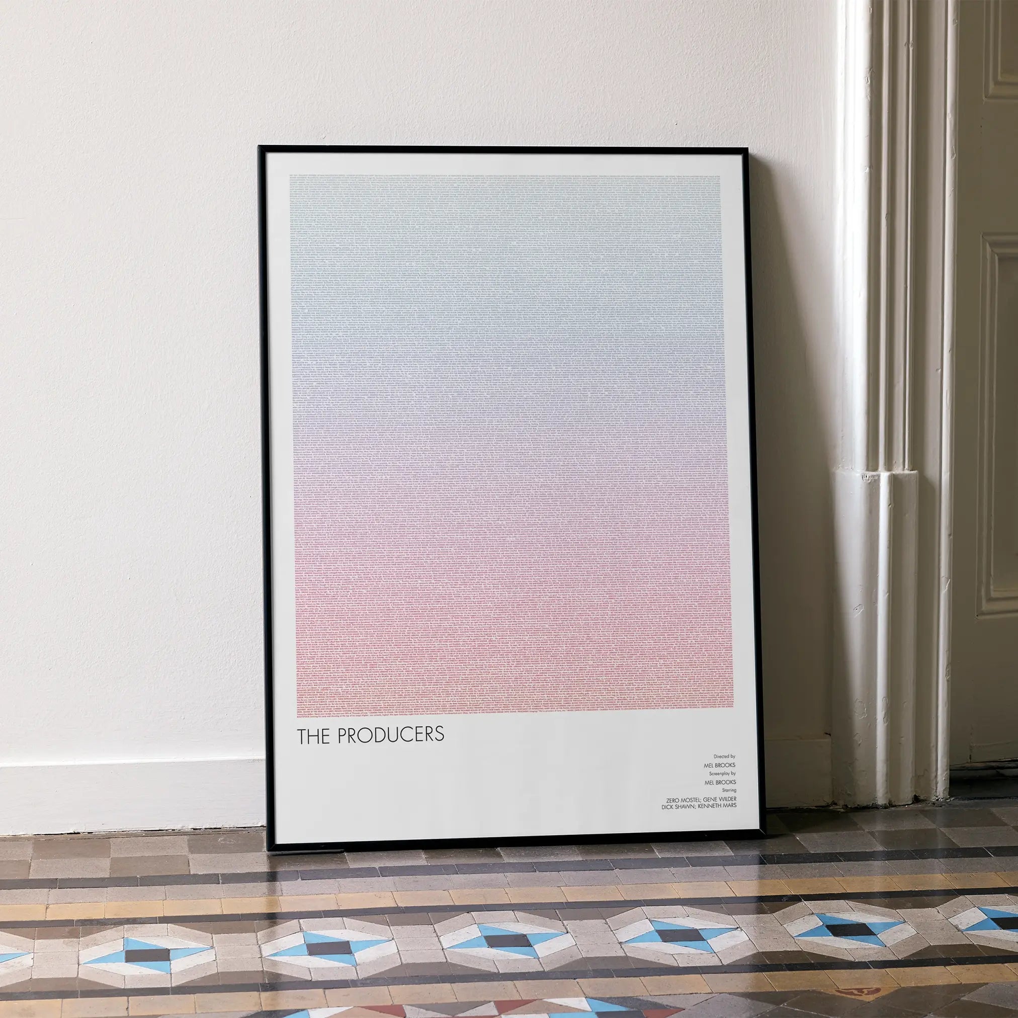 A framed The Producers movie script poster leaning against a wall in a minimalist interior.