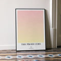 A framed The Producers movie script poster leaning against a wall in a minimalist interior.